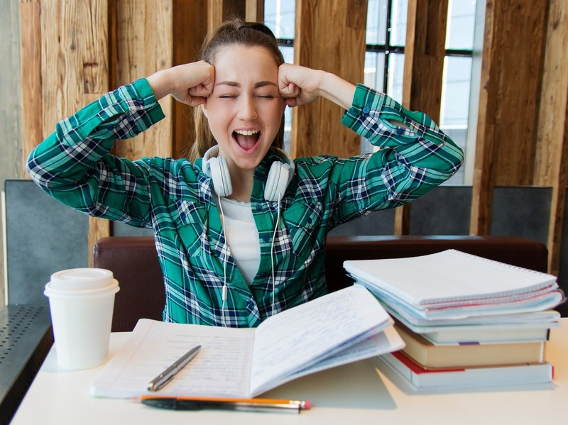 Das Bild zeigt eine Studentin, die vor Büchern sitzt und sich beide Fäuste an die Schläfen drückt.