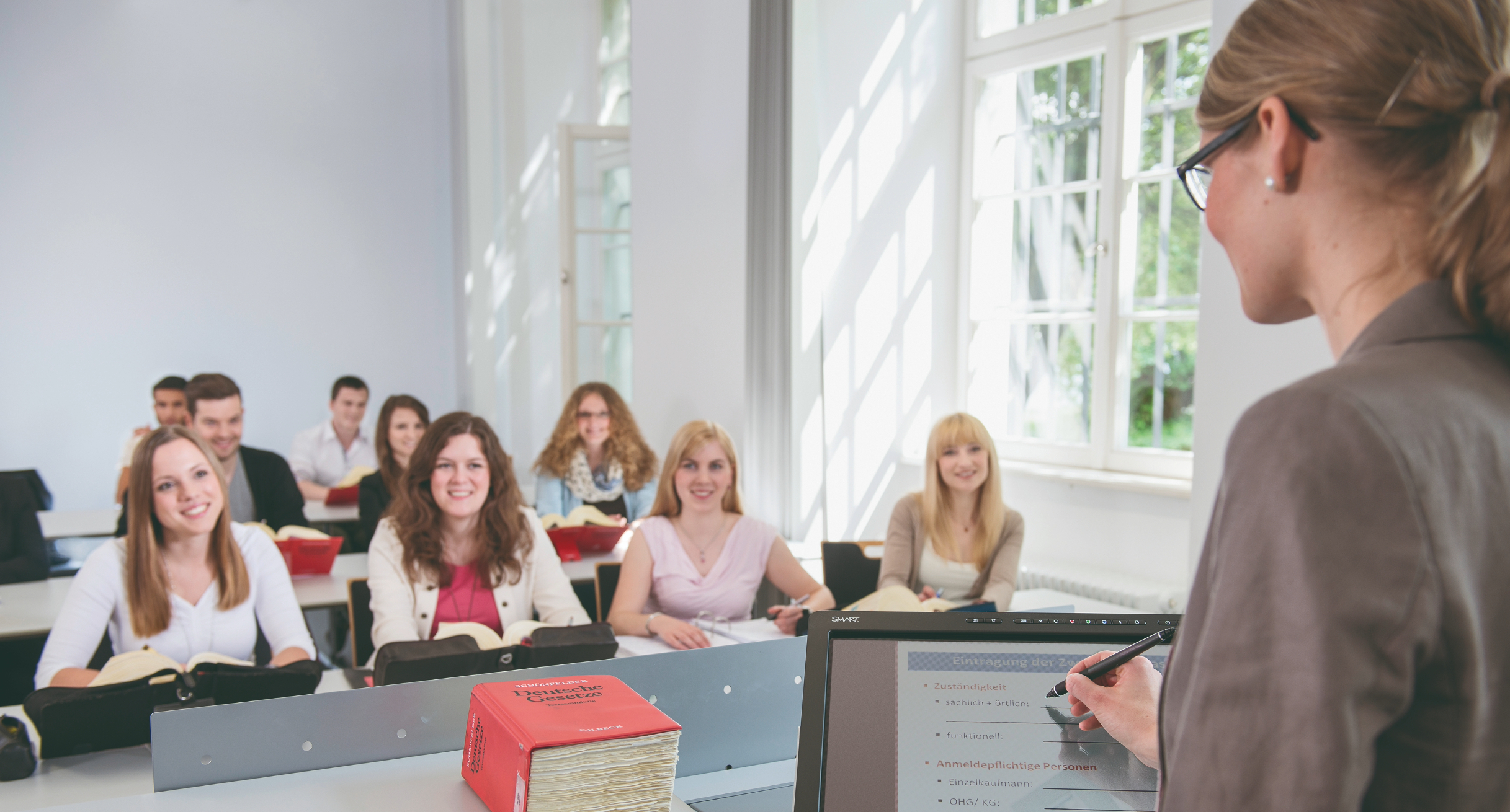Das Bild zeigt eine Dozentin, die in Hörsaal vor Studierenden am SMART-Podium steht.