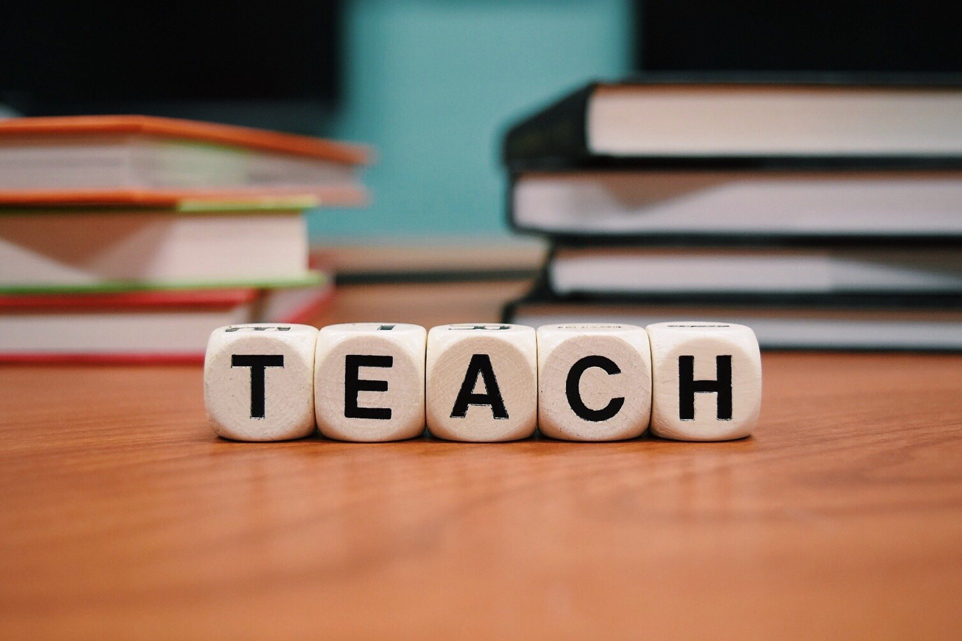 Das Bild zeigt fünf Würfel mit Buchstaben. Sie bilden zusammen das Wort TEACH.