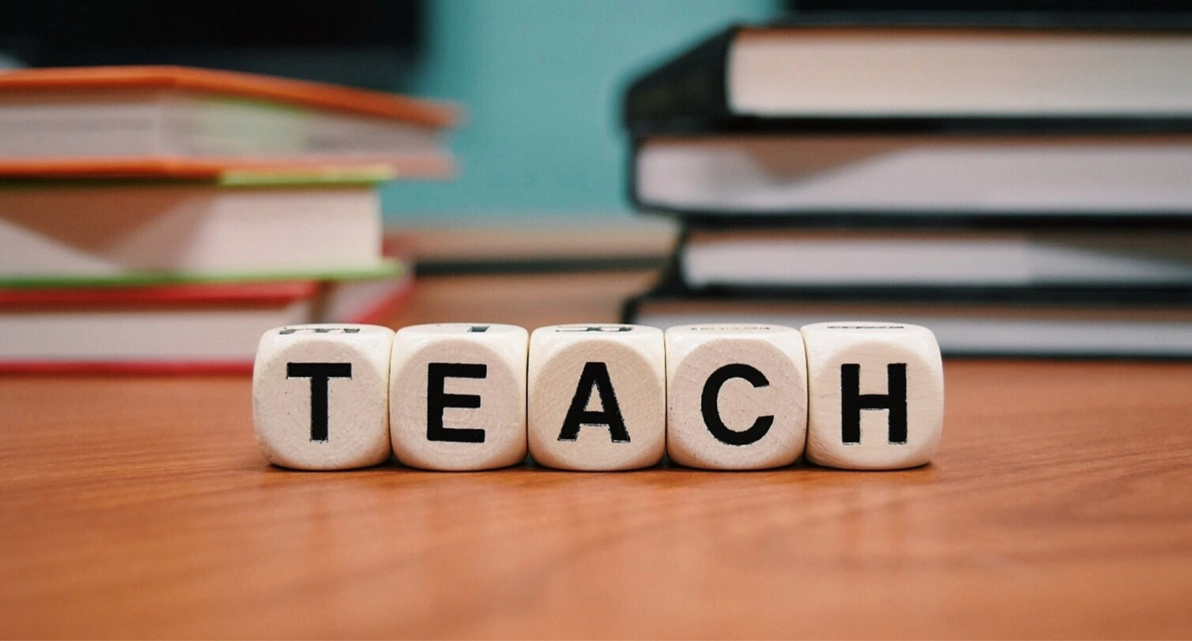 Das Bild zeigt fünf Würfel mit Buchstaben. Sie bilden zusammen das Wort TEACH.