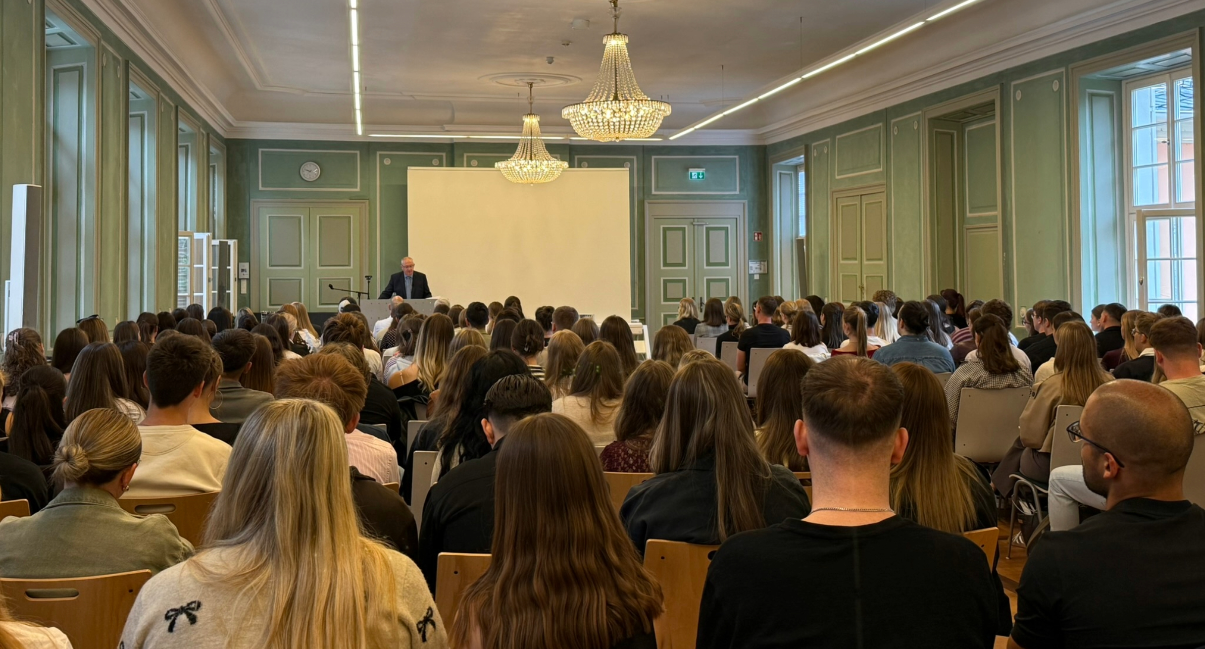 Studierende sitzen in der Aula der HfR Schwetzingen während der Prorektor sie begrüßt
