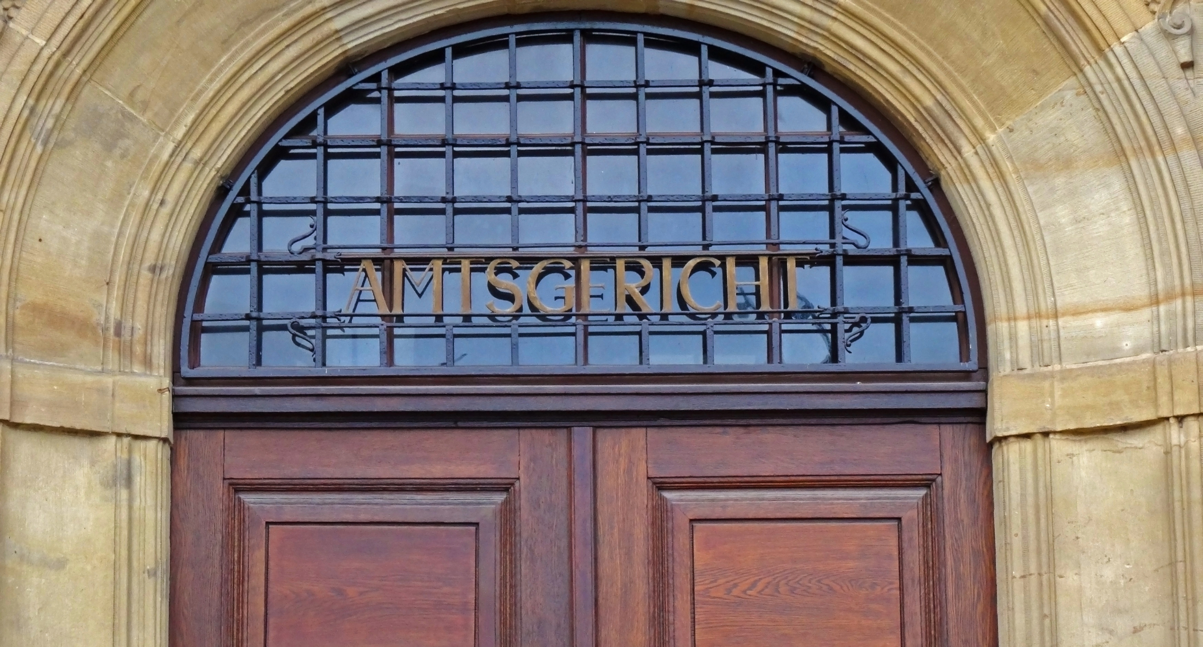 Obere Teil einer braunen Holztür. Über der Tür steht das Wort Amtsgericht.
