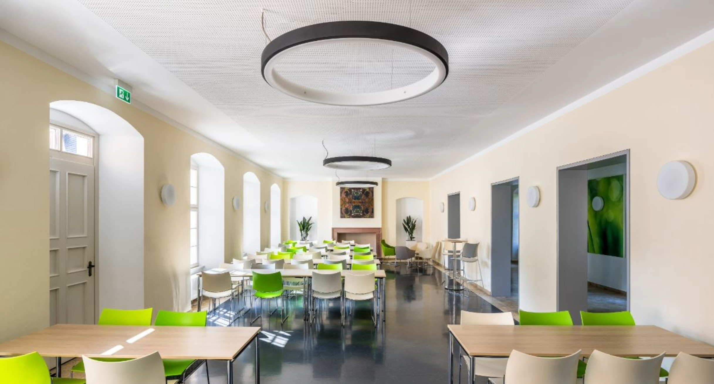 Cafeteria der Hochschule am Studienort Schwetzingen. Helle Tische mit hellgrünen, dunkelgrünen und beigefarbenen Stühlen.